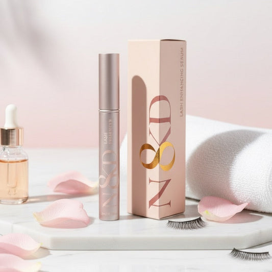 Makeup products including a enhancing serum tube, box, and eyelash on a light pink background